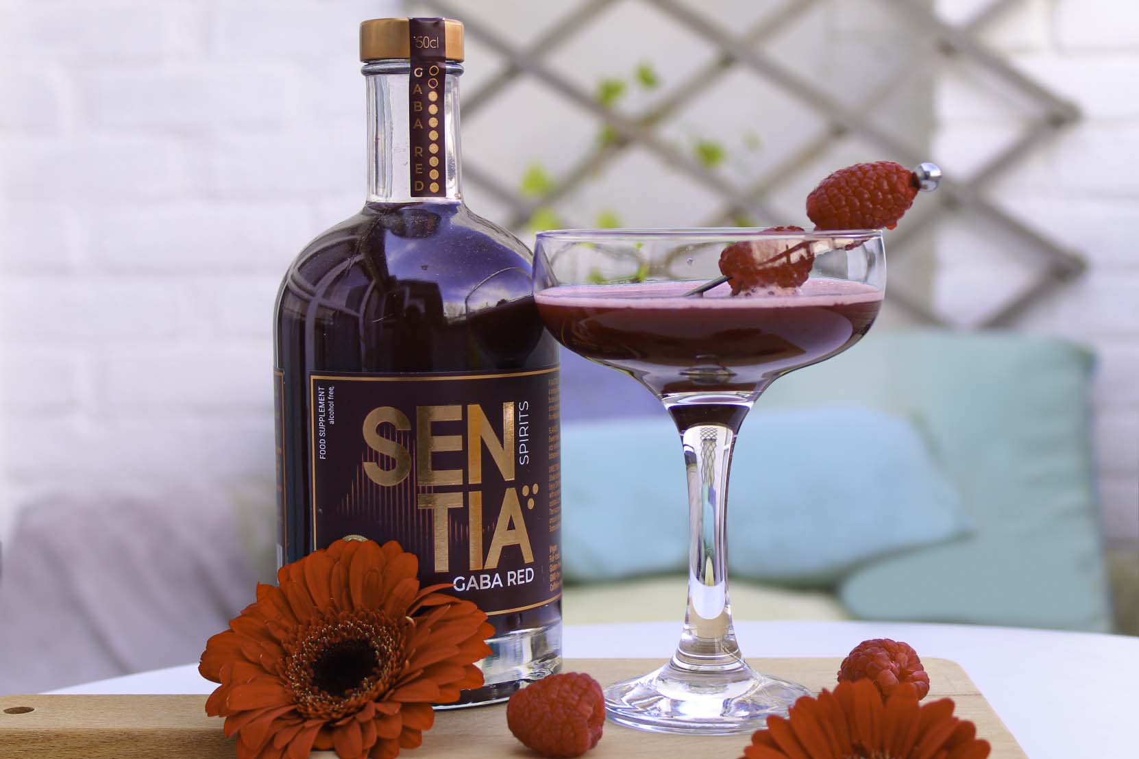 Image of the Raspberry Sentini with red flowers laying around it for decor, and a bottle of Sentia Red next to it.