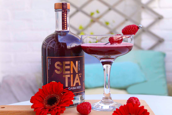 Image of the Raspberry Sentini with red flowers laying around it for decor, and a bottle of Sentia Red next to it.