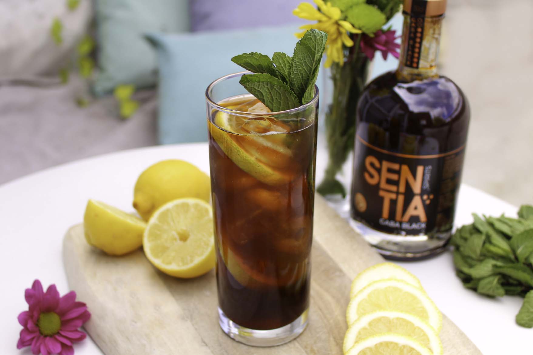 Image of the Iced Tea with lemon and floral decor and a bottle of GABA Black in the background.